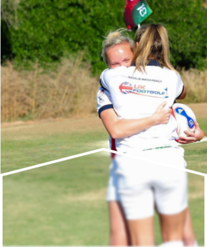 Two female footgolf players embracing on a golf course.