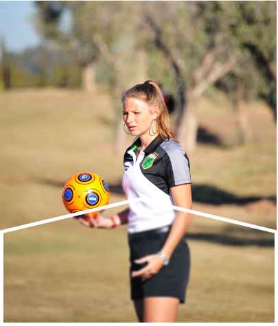 A female player holding a yellow soccer ball is standing on a golf course.