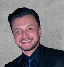 A portrait photo of a smiling man in a black suit and a blue shirt.