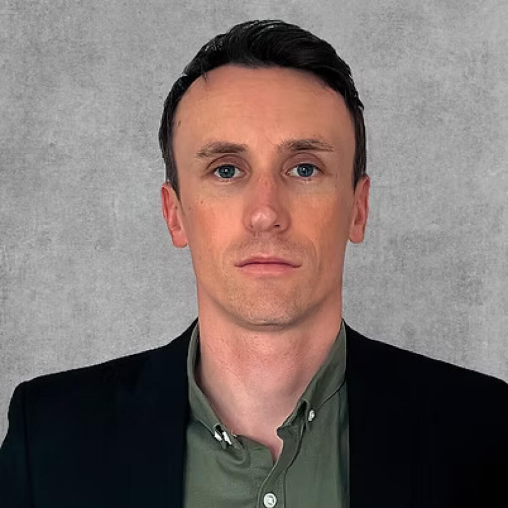 A Portrait photo of a man in a black suit and a green shirt.