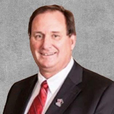 A portrait photo of a smiling man in a black suit and a red tie.