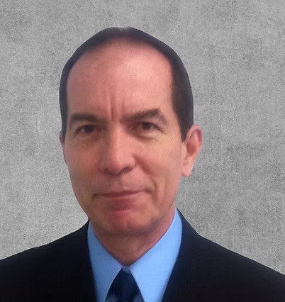 A portrait photo of a smiling man in a dark suit and a blue shirt.