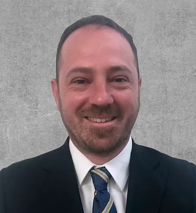 A portrait photo of a smiling man in a dark suit and a blue tie.