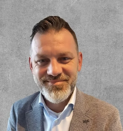 A headshot of a man in a gray suit in front of a wall.