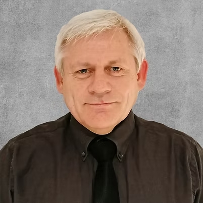 A close-up headshot of a man in a dark brown shirt and a tie.