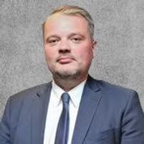 A headshot of a man in a dark grey suit.