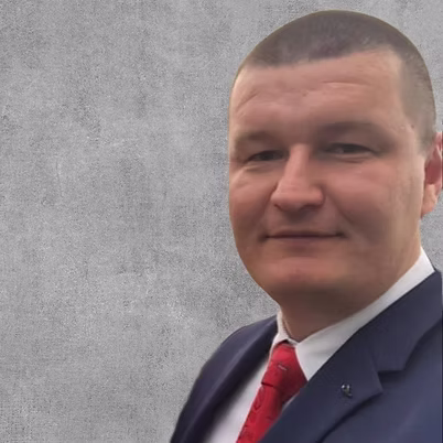 A man in a blue suit and a red tie standing in front of a wall.
